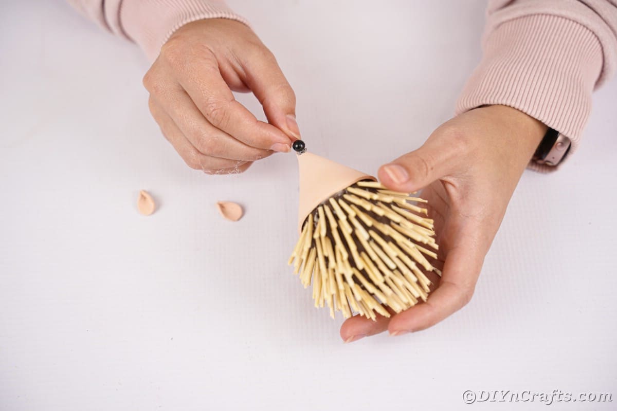 Hand putting bead on nose of hedgehog toy