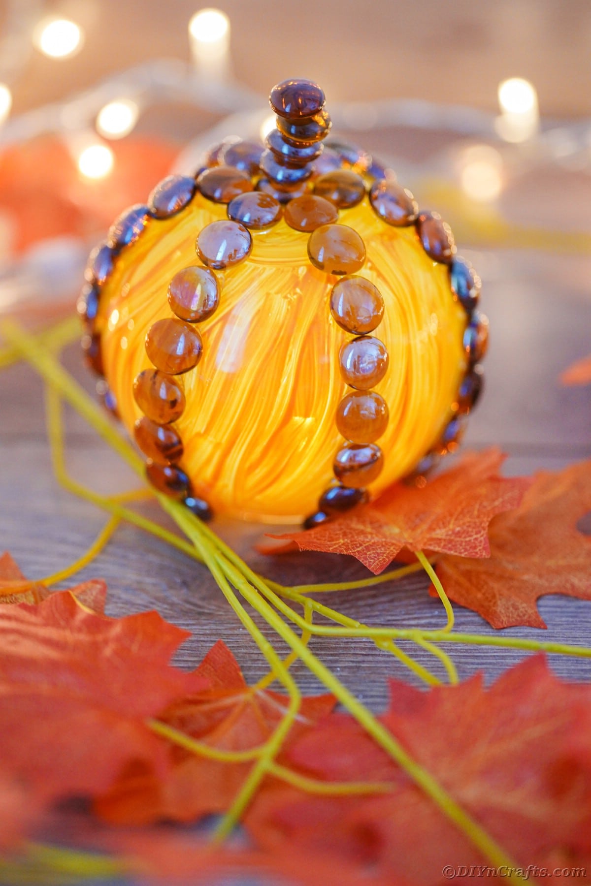 Painted glass pumpkin on table with lights in background