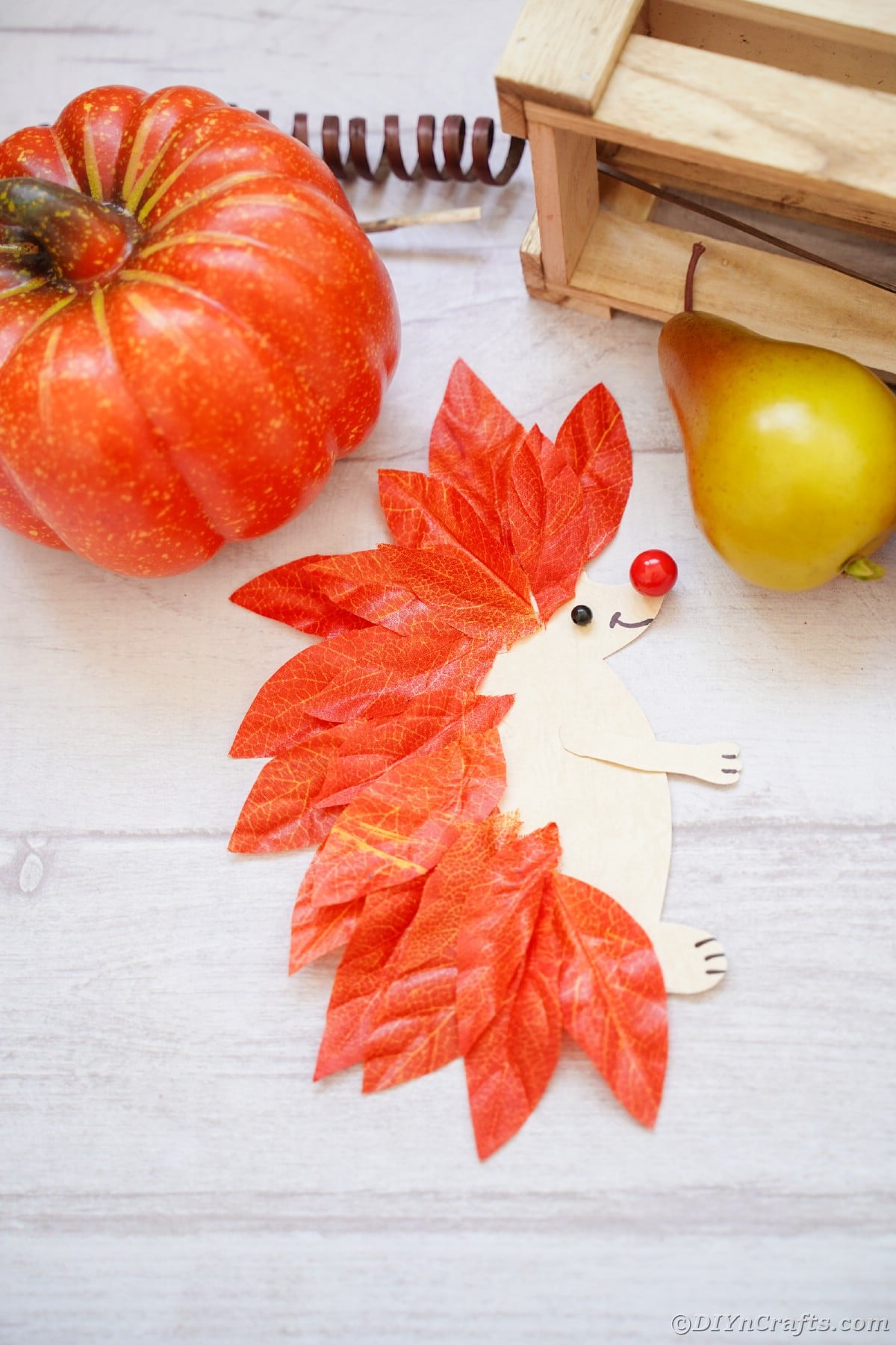 Paper and leaf hedgehog laying on white wood slat