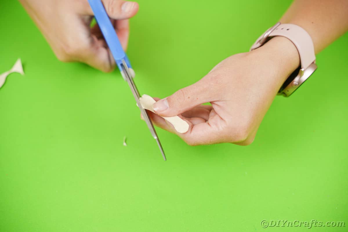 Hand holding blue scissors trimming cream paper