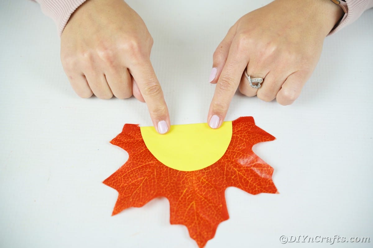 Hände, die gelben Papierkreis auf künstlichem Orangenblatt halten