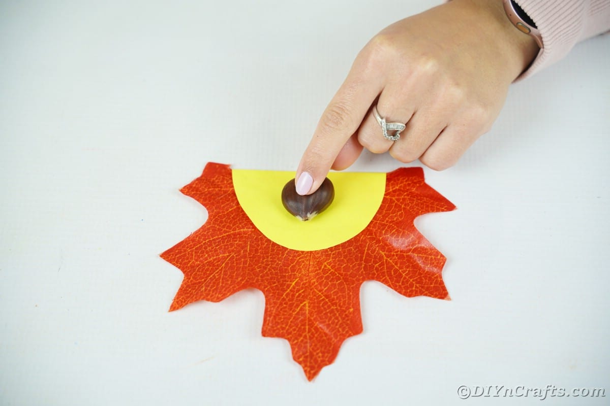 Hand gluing nut shell on yellow paper on leaf