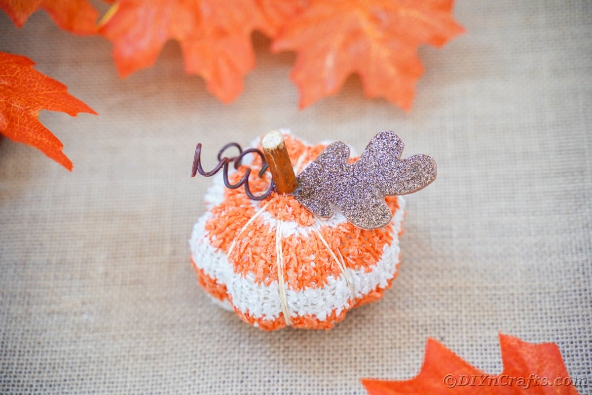 Fabric pumpkin on brown table with fake leaves