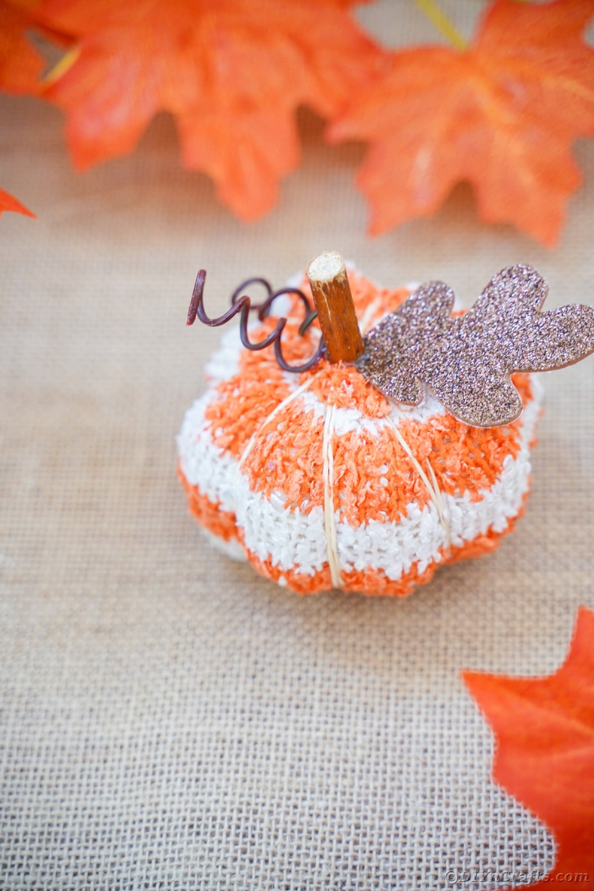 Striped fabric pumpkin on tan burlap with fake leaves