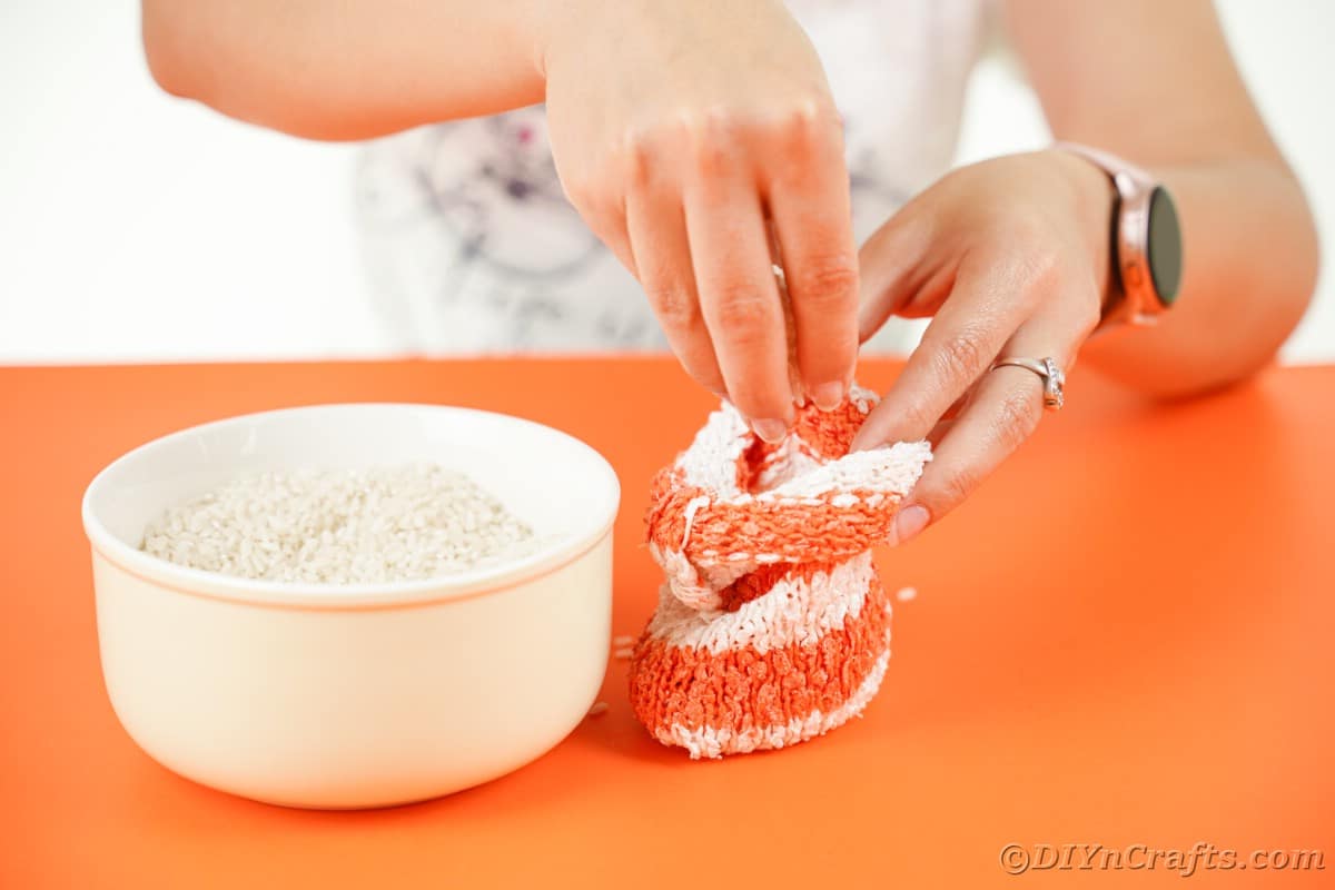 Hand stuffing rice into orange and white striped sock