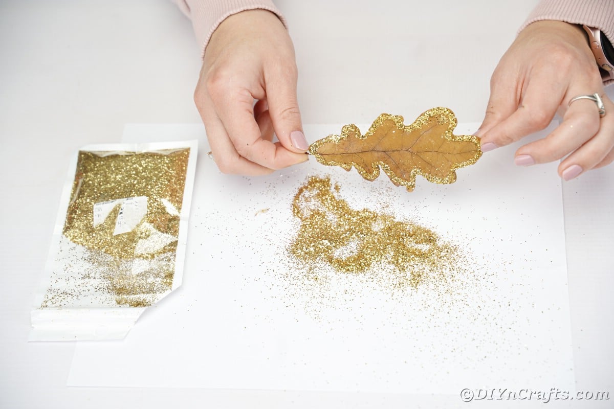 Holding leaf above pile of glitter on white table