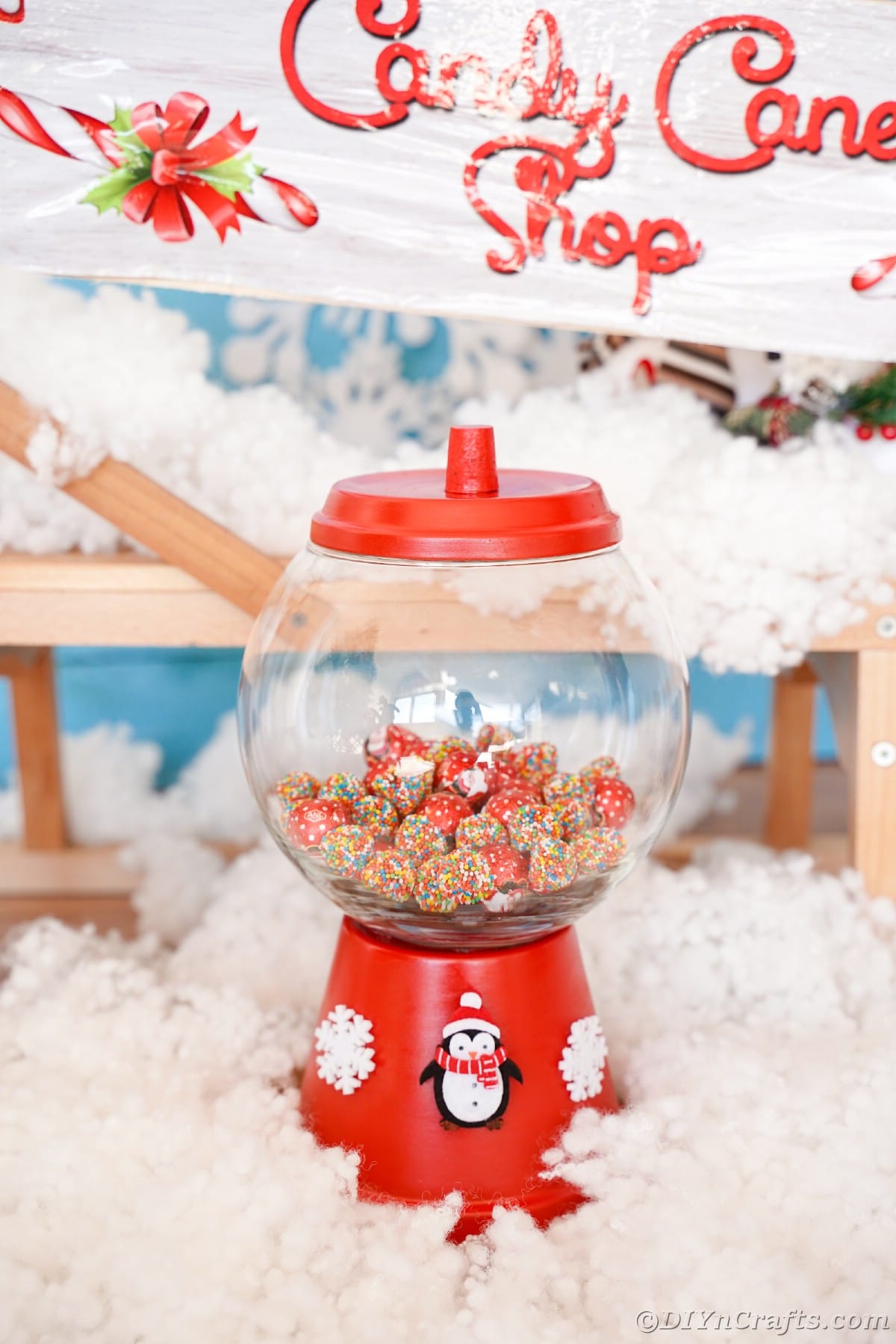 red candy jar on fake snow with candy cane shop sign in background