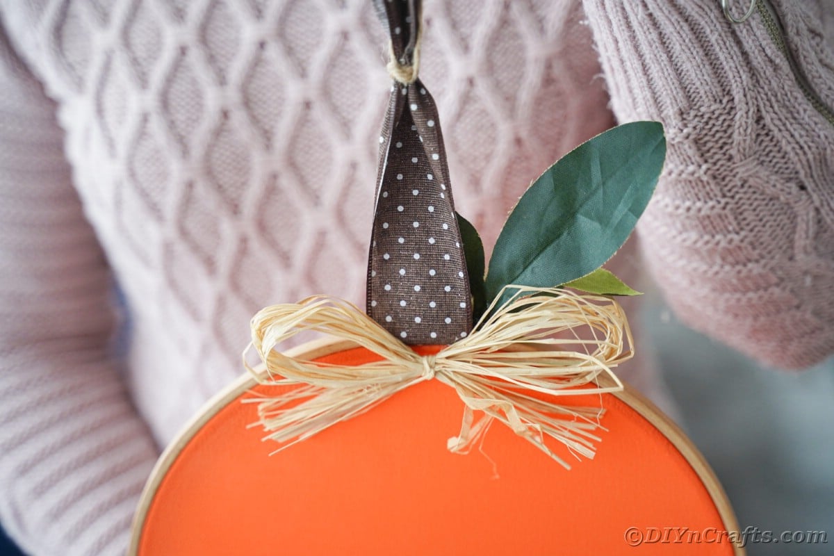 top of pumpkin with brown polka dot ribbon stem held by woman