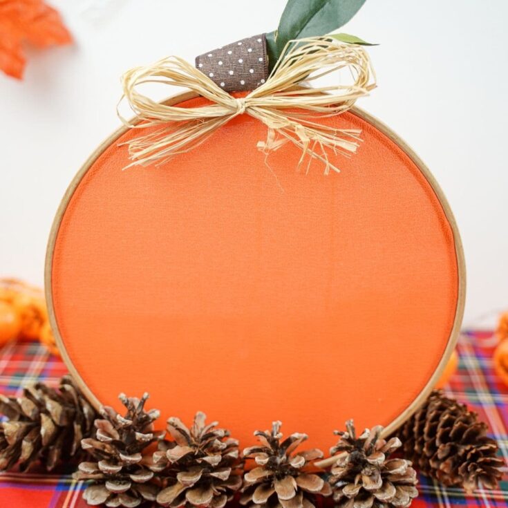 fabric pumpkin on plaid cloth with pinecones around the bottom