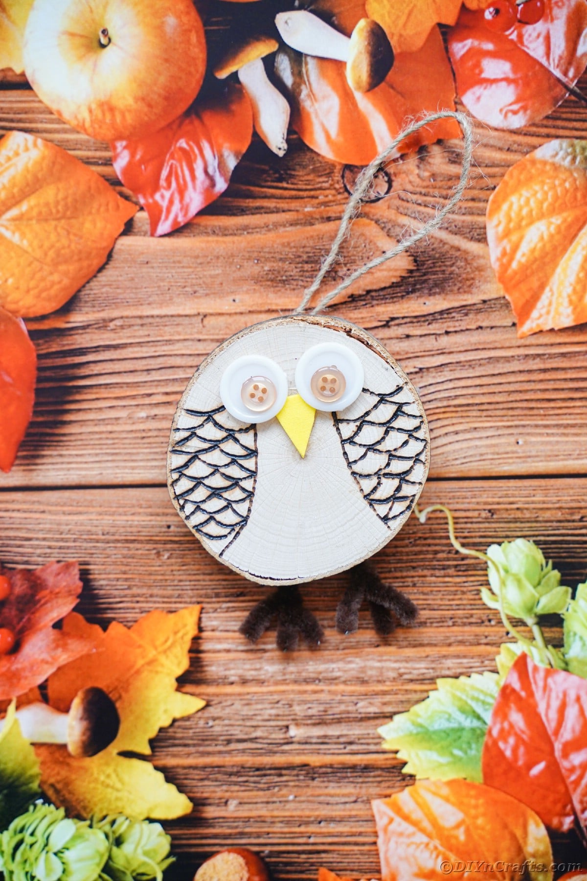 Wood slice owl with twine hanger laying on wood with fall leaves