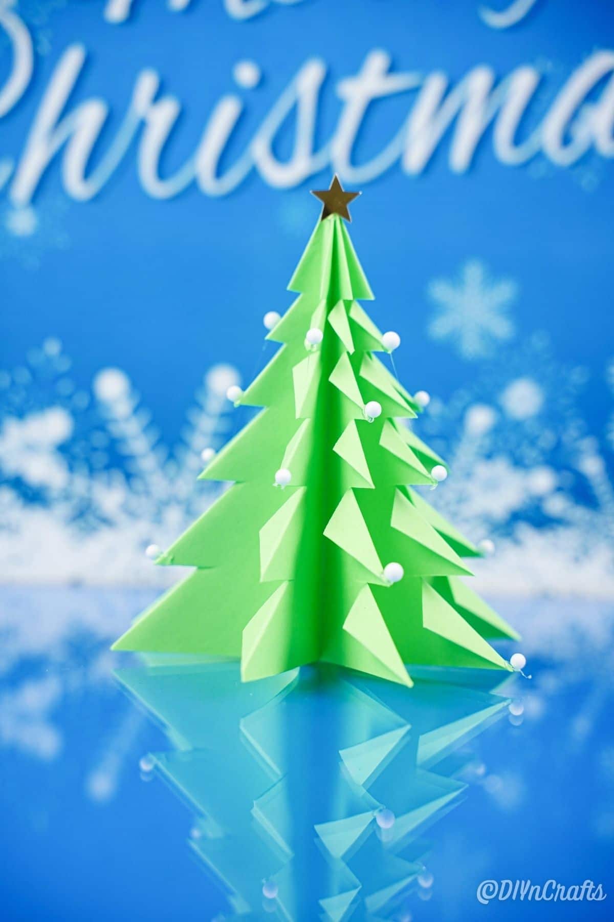 papirnato 3d božično drevo na modri površini s ponarejenim snežnim ozadjem