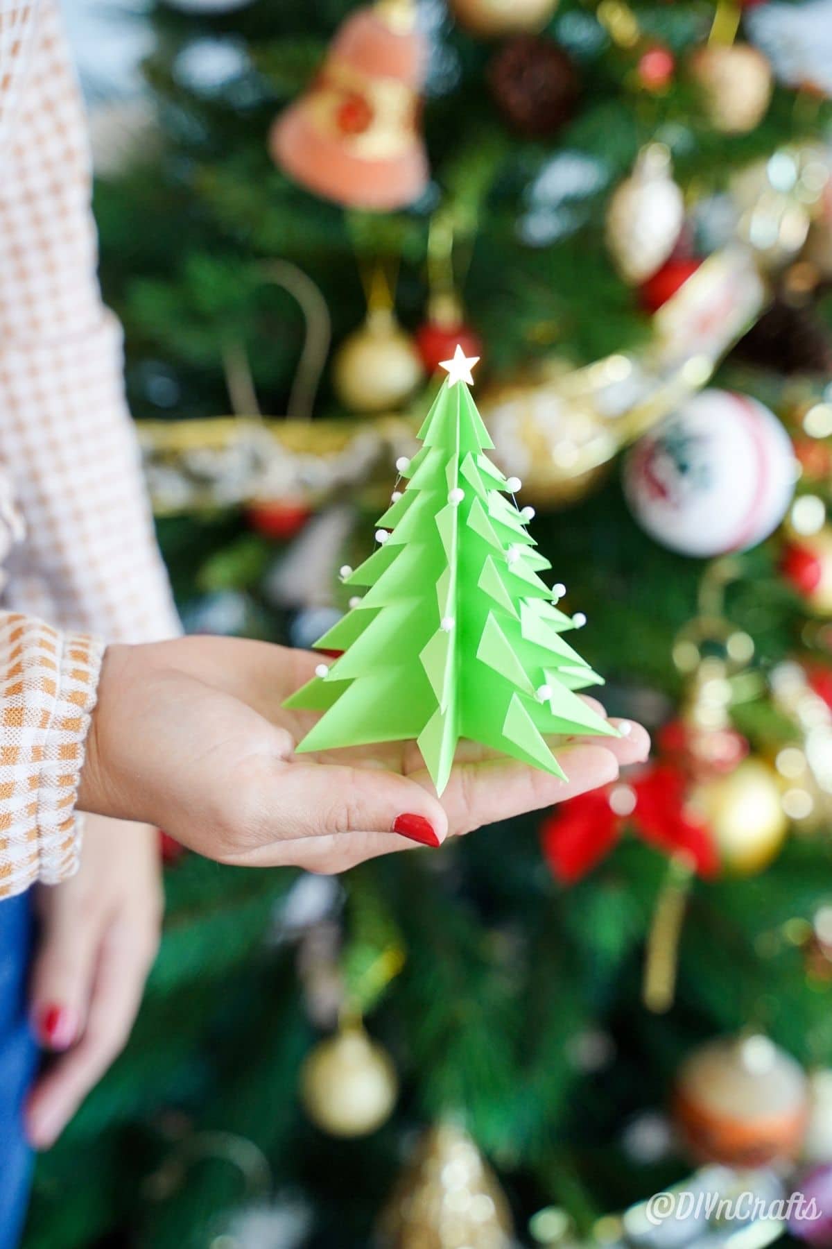 woman holding green paper tree in front of decorated Christmas tree
