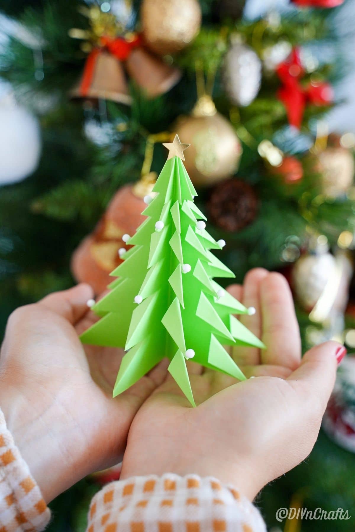 mains tenant un sapin de Noël en papier vert
