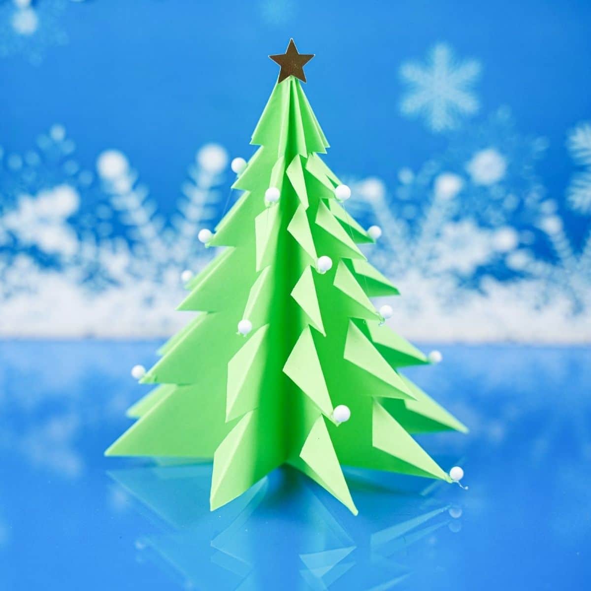 blue snow background behind green paper tree