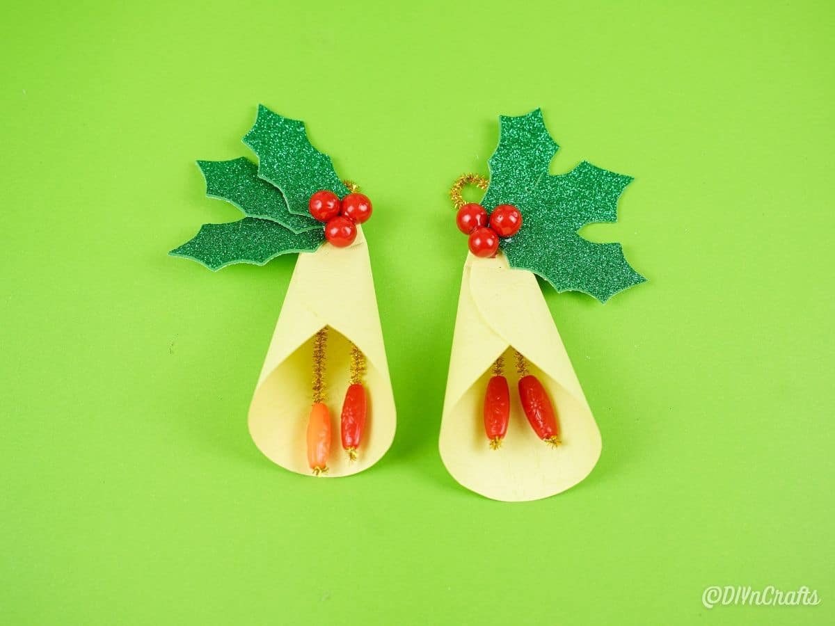 two yellow bells with holly on green paper
