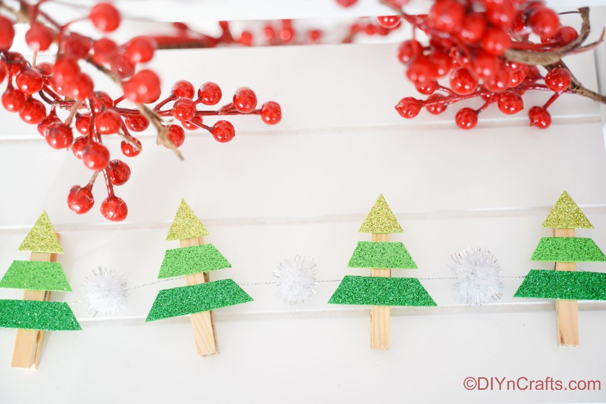 green clothespin tree garland on white board with fake berries