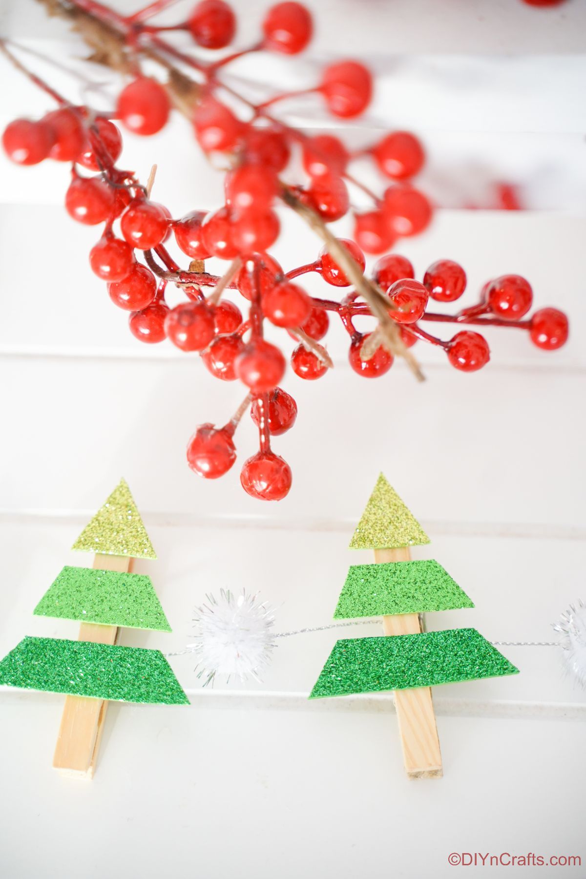 two clothespin mini trees on white shiplap with red fake berries hanging above
