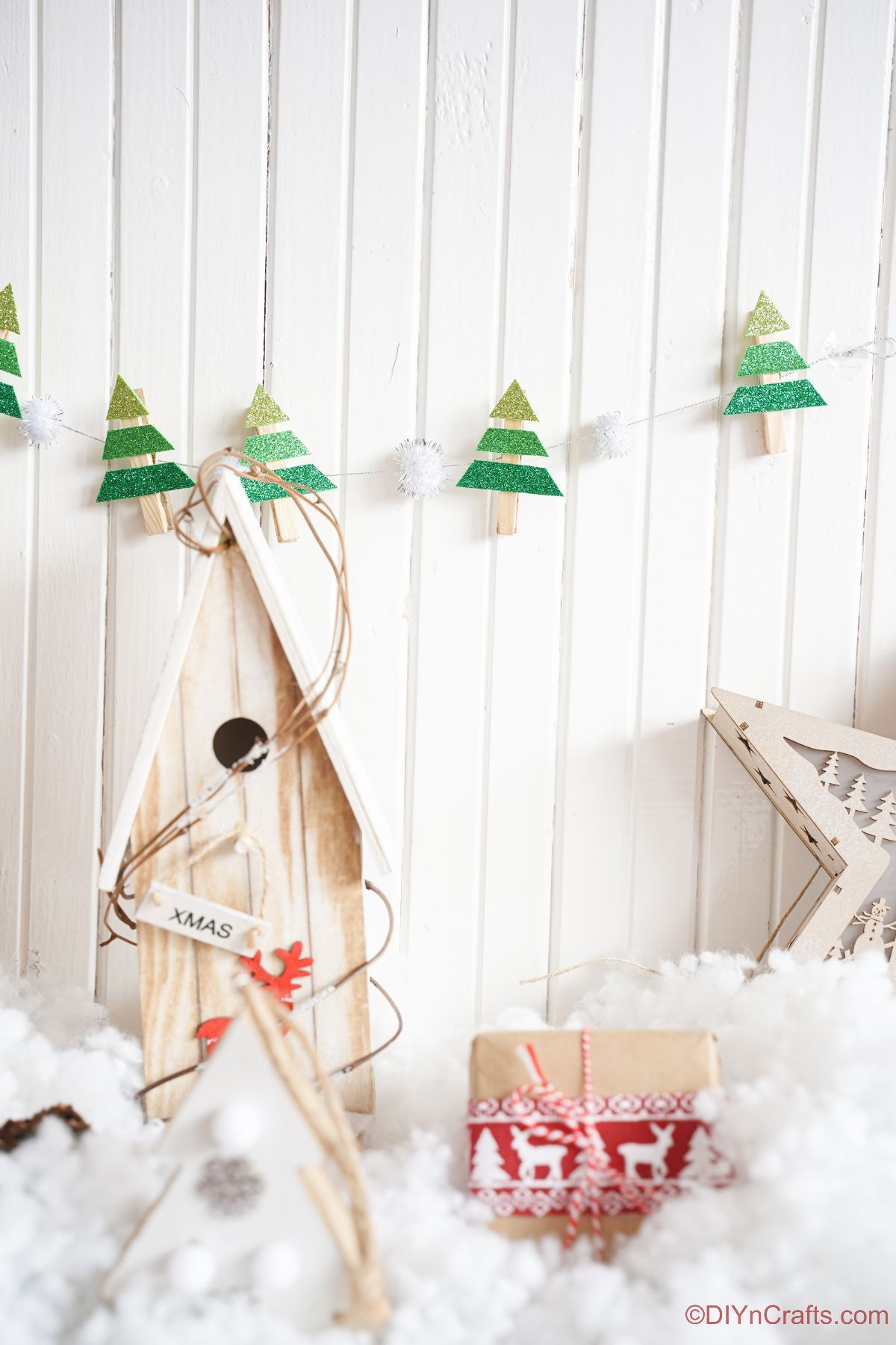 mini tree garland hanging on white wall above holiday decor and fake snow