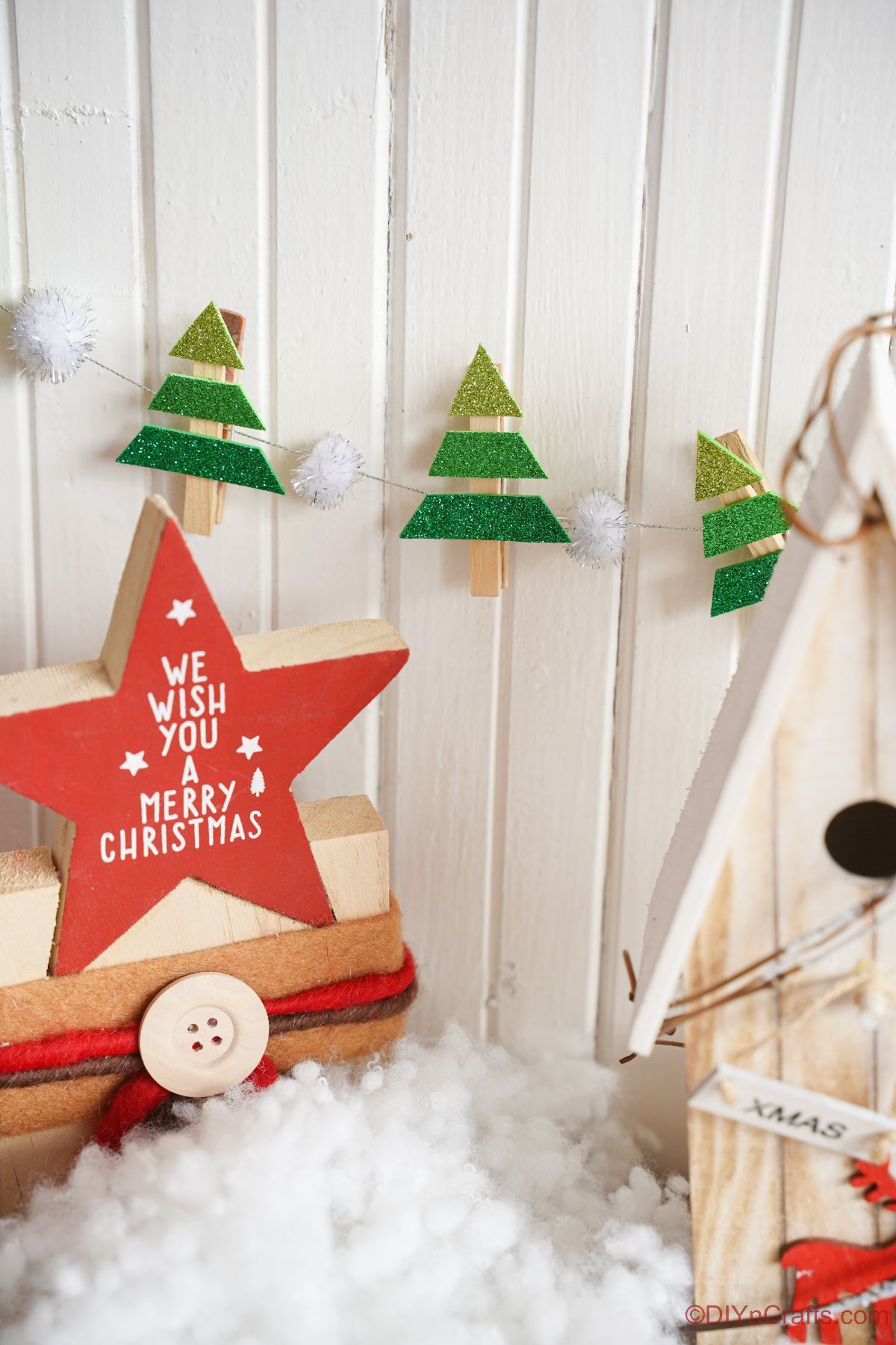 mini foam christmas tree on clothespins hanging on white shiplap behind holiday star decoration
