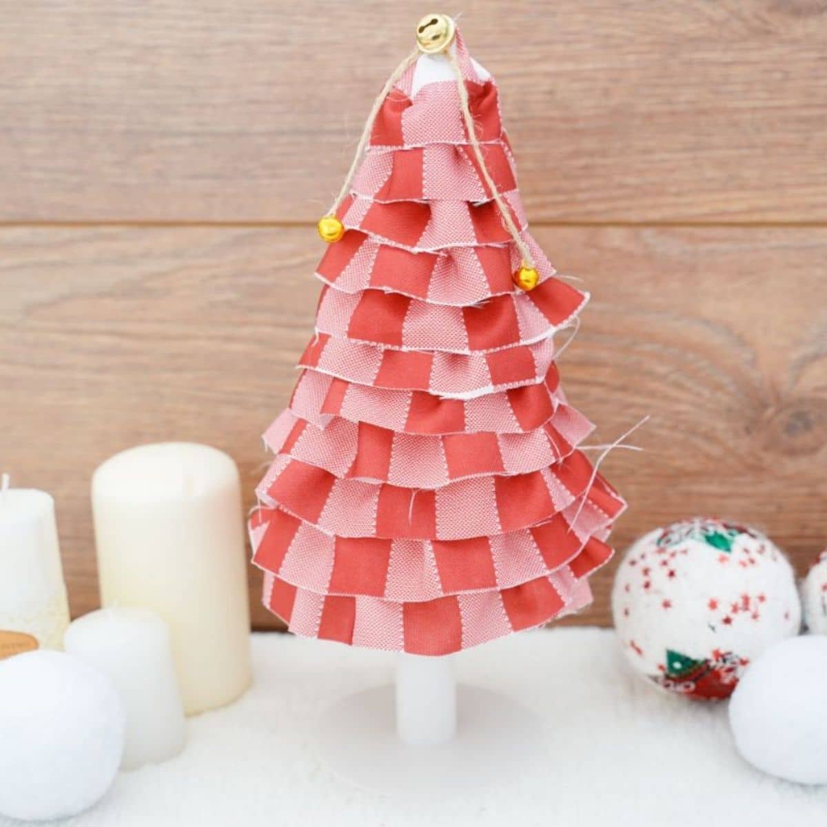 miniature holiday tree with red fabric on white table with candles on the side