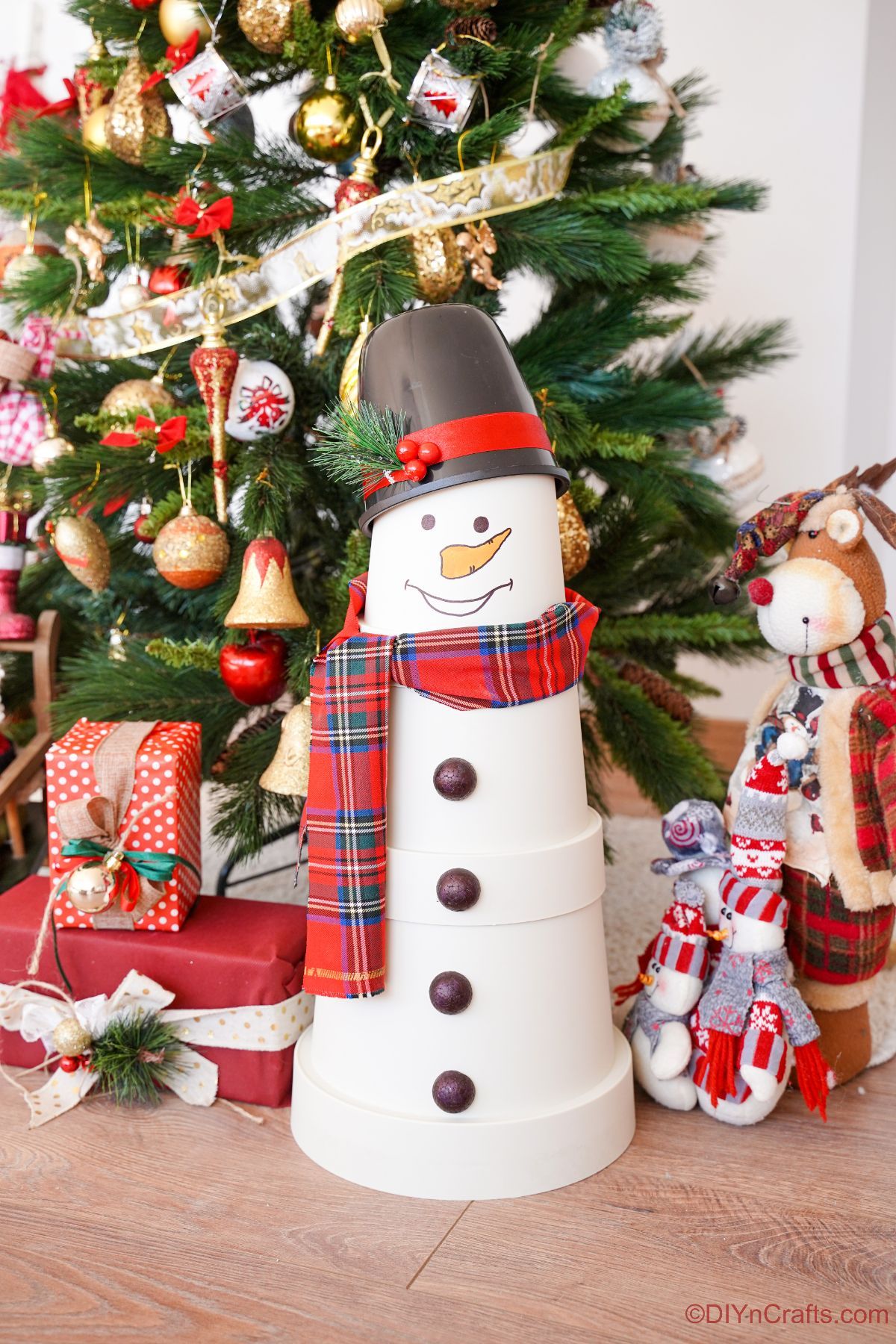 fake flower pot snowman in front of Christmas tree with presents