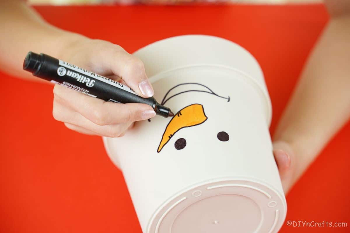 hand outlining orange nose shape on white flower pot with black marker