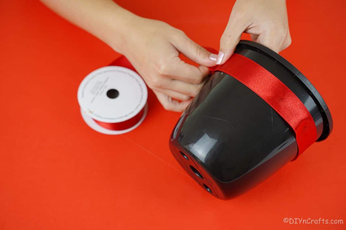 hand gluing red ribbon onto black bucket edge