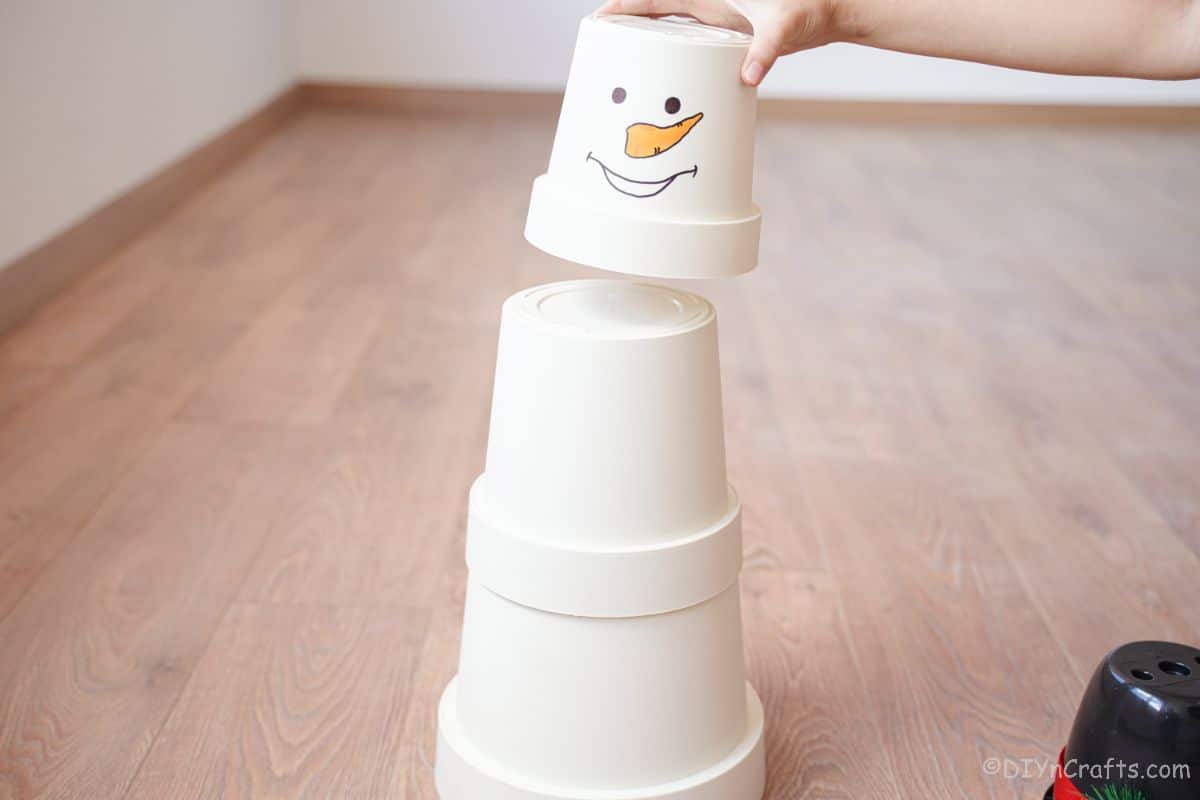 hand stacking white flower pots on top of each other with one with face on top