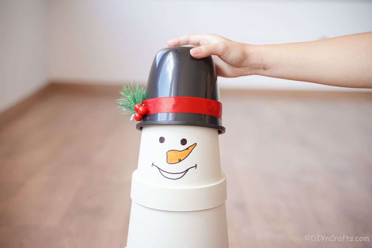 roka drži črni klobuk na vrhu cvetličnega lonca snežaka