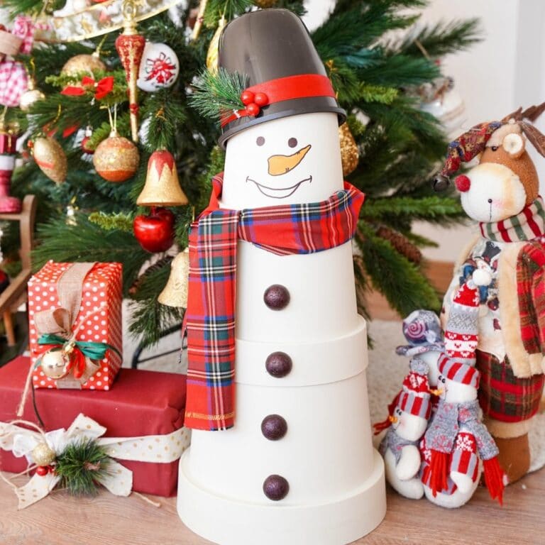 fake flower pot snowman in front of Christmas tree with presents