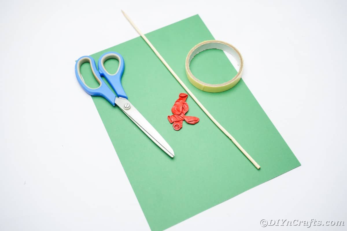 green paper red balloons scissors and a dowel on white table