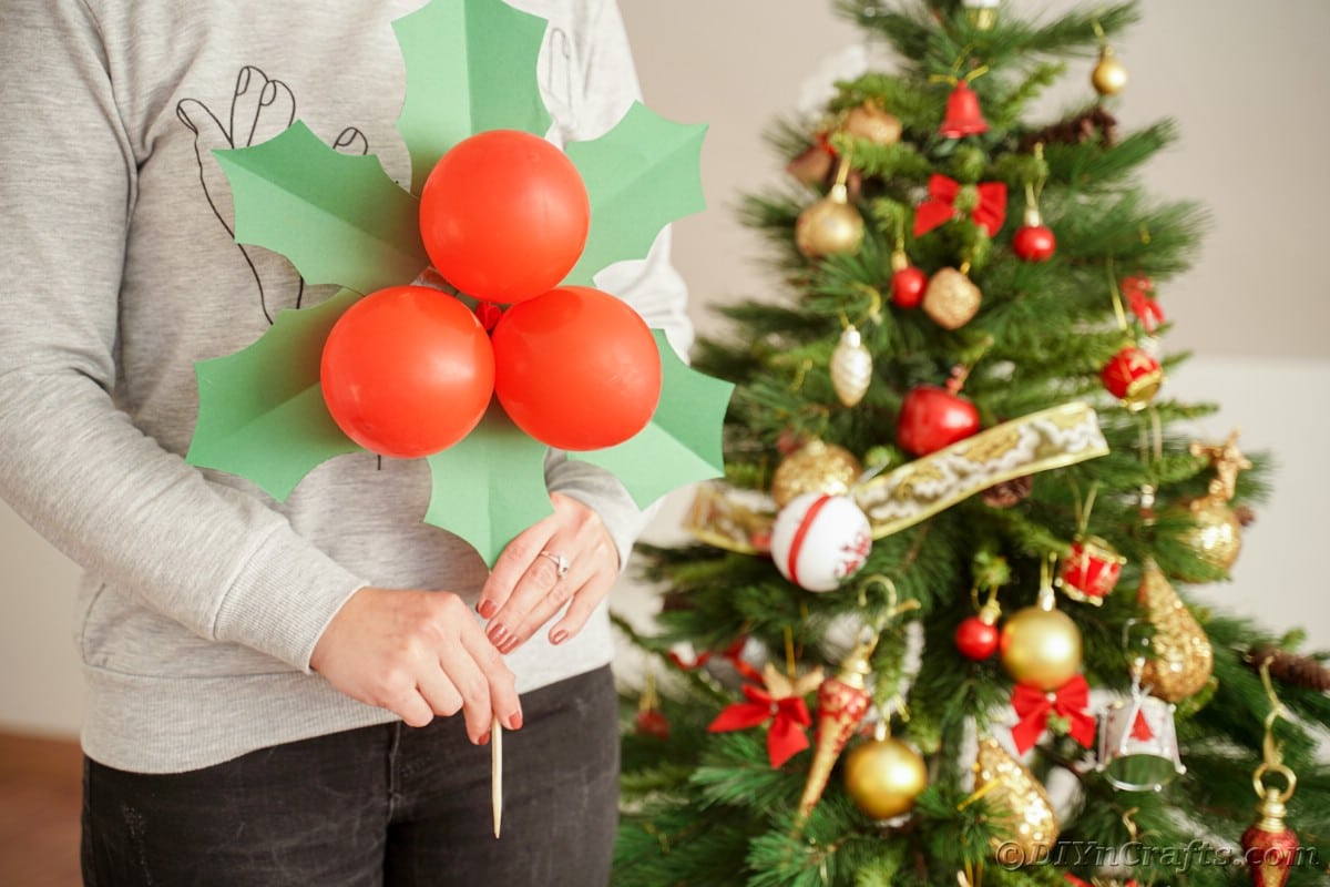 lady in black pants holding giant holly leaf and berries decoration