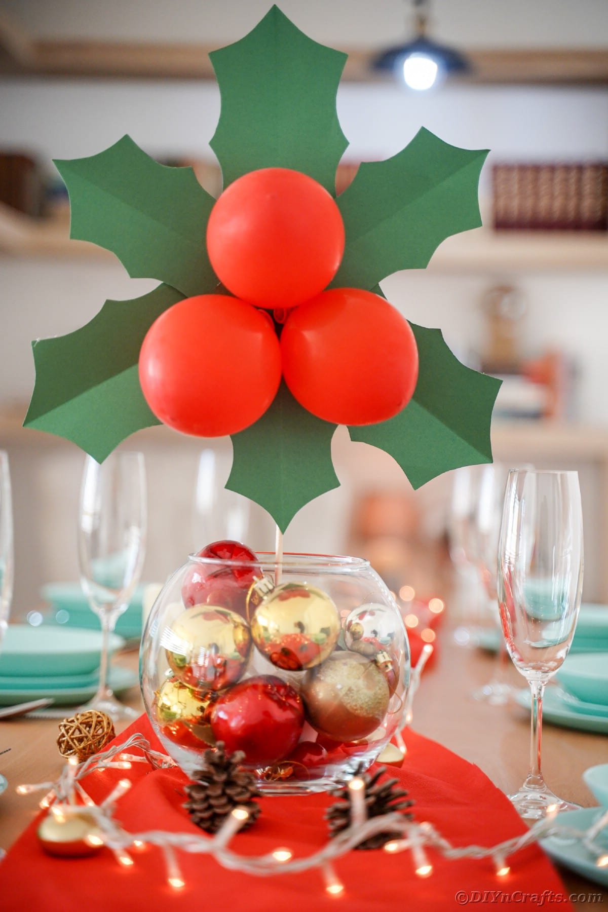 steklena skleda z zlatimi in rdečimi okraski na mizi, ki drži velikanske liste božikovine