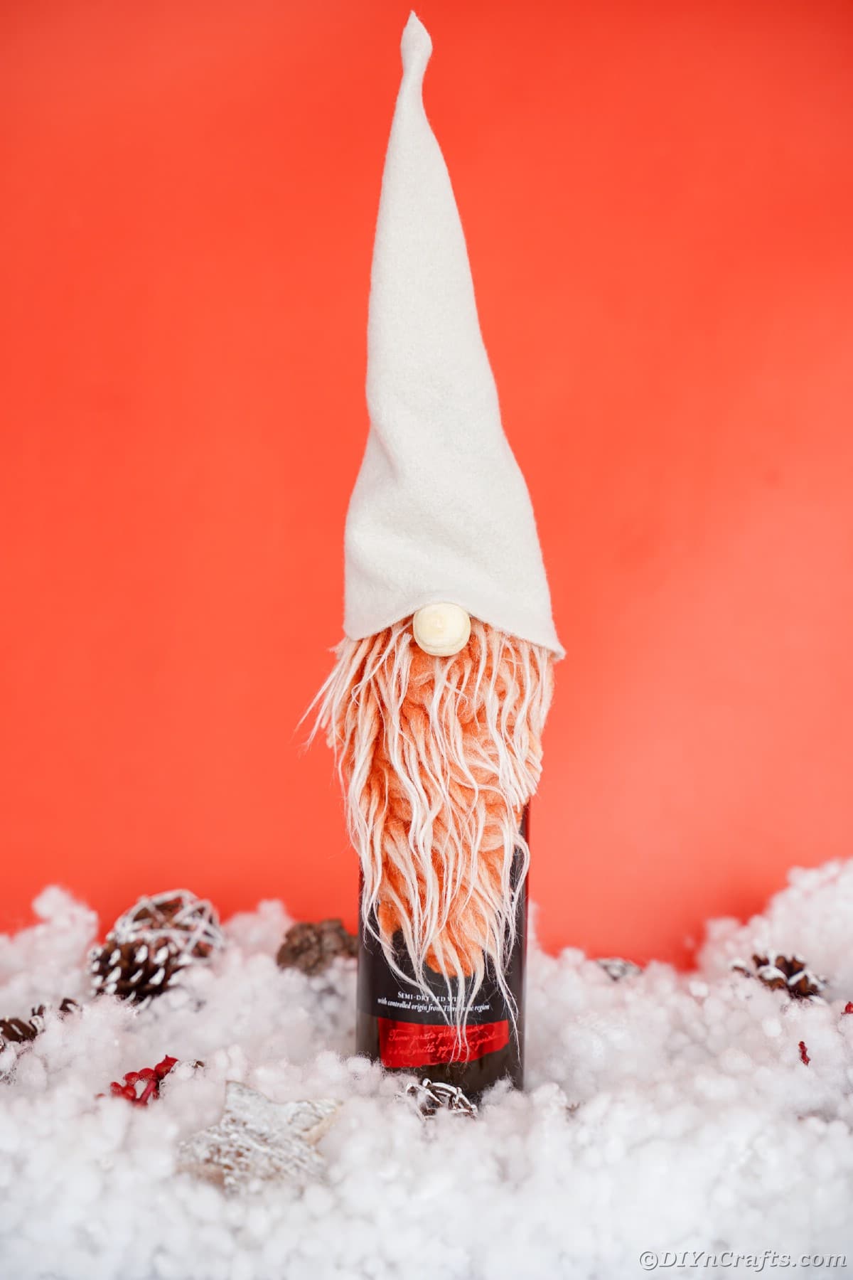 gnome on top of wine bottle sitting on fake snow with red background