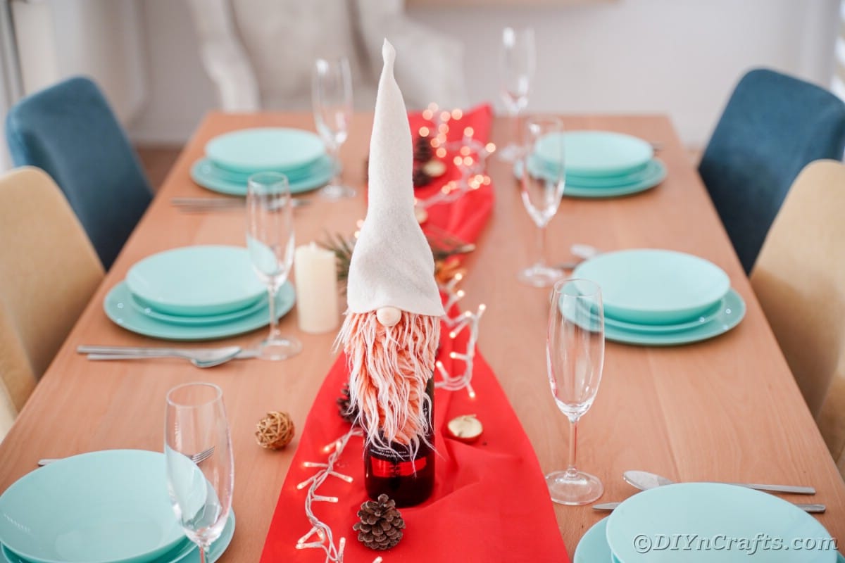 teal place settings with red table runner holding gnome on wine bottle