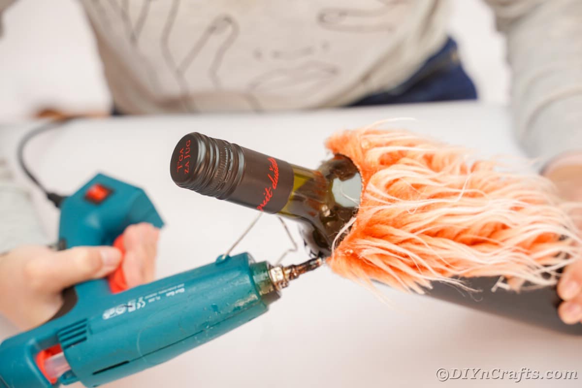 gluing orange fake fur on wine bottle