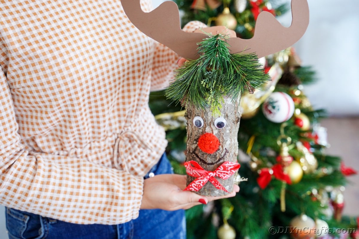 lady holding log reindeer in front of christmas tree