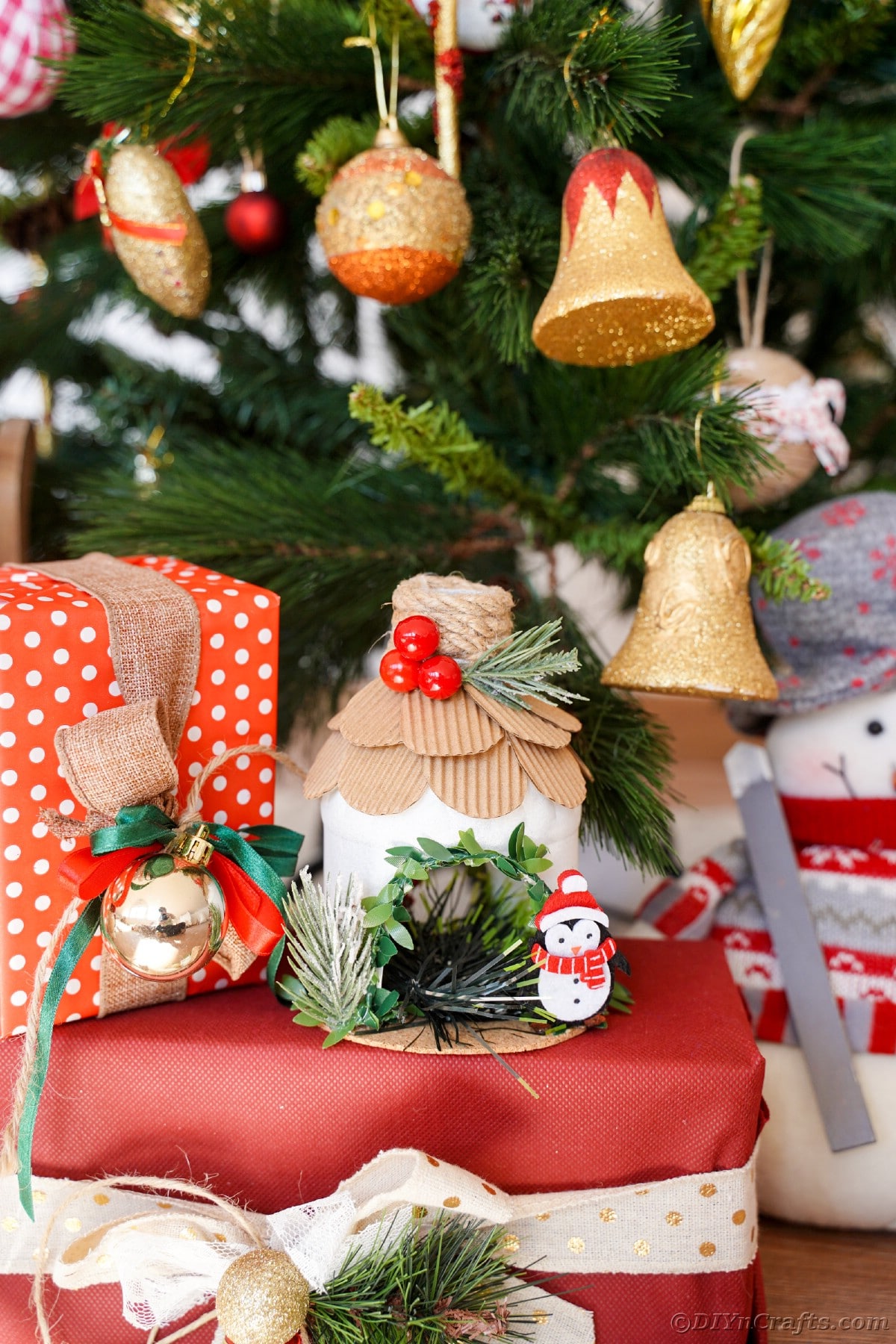 Christmas tree with bell ornaments in background with red and white polka dot and solid red boxes in front of tree