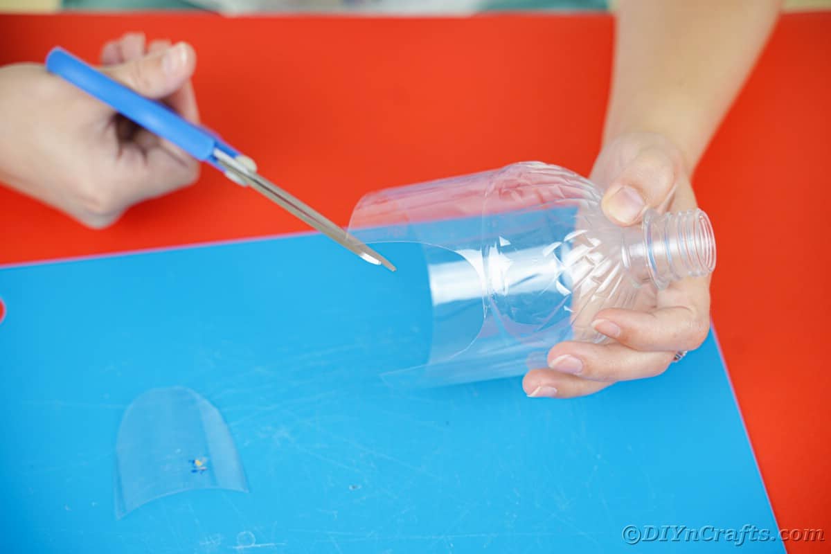 blue scissors being used to cut doors on side of plastic bottle