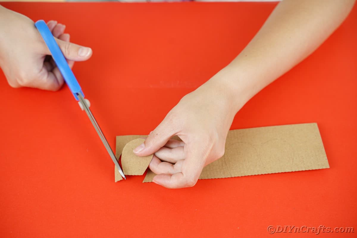 ladies hand using blue scissors to cut out cardboard shingles