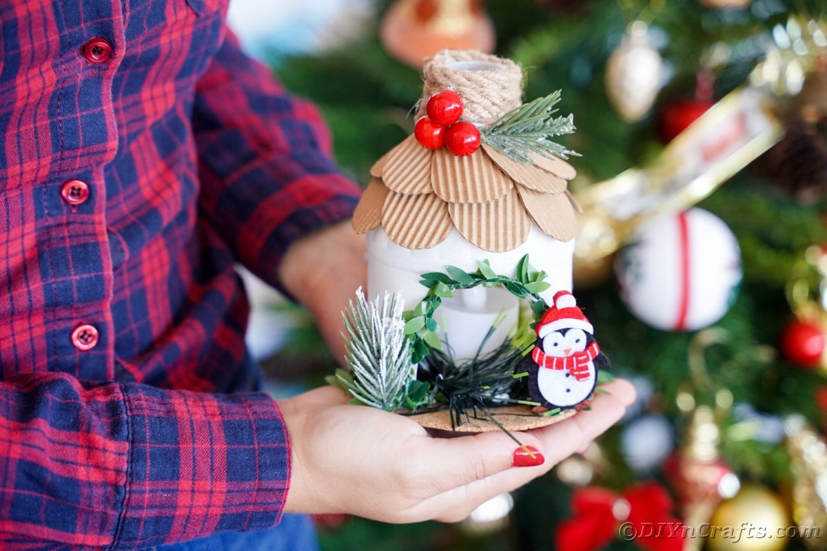 lady in blue and pink plaid shirt holding miniature north pole hosue in front of Christmas tree