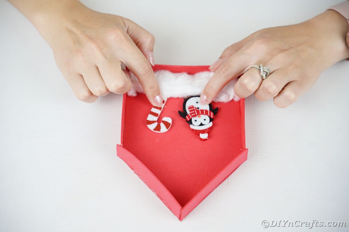 hands holding mini penguin and candy cane on red foam house