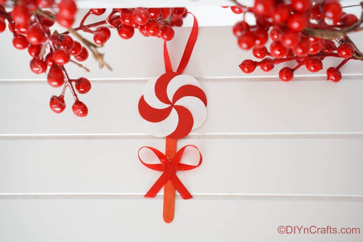 peppermint candy ornament hanging against white wall with fake berries