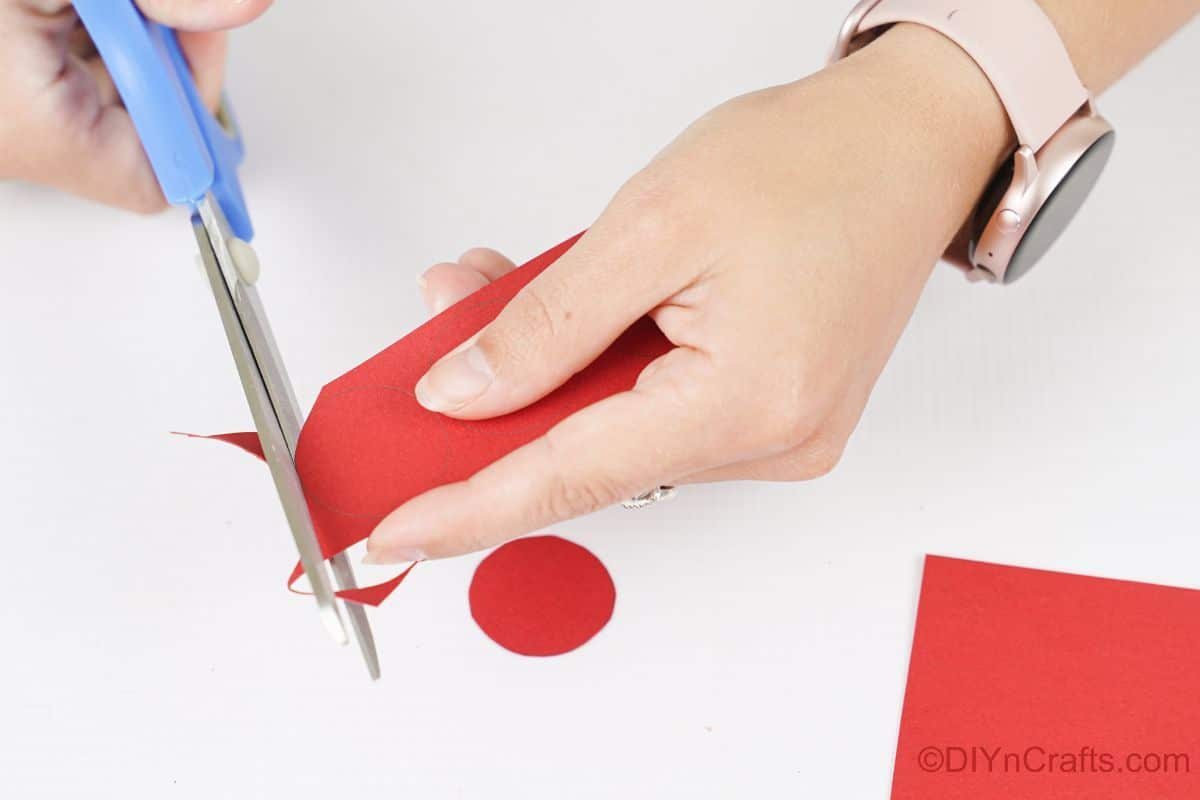 hand holding blue scissors cutting circles from red paper