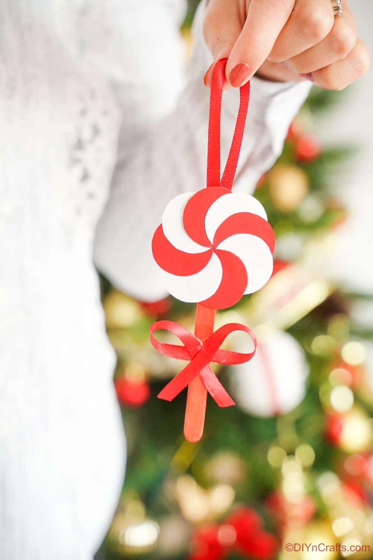 Dame en pull blanc tenant l'ornement de bonbons à la menthe poivrée devant l'arbre de Noël