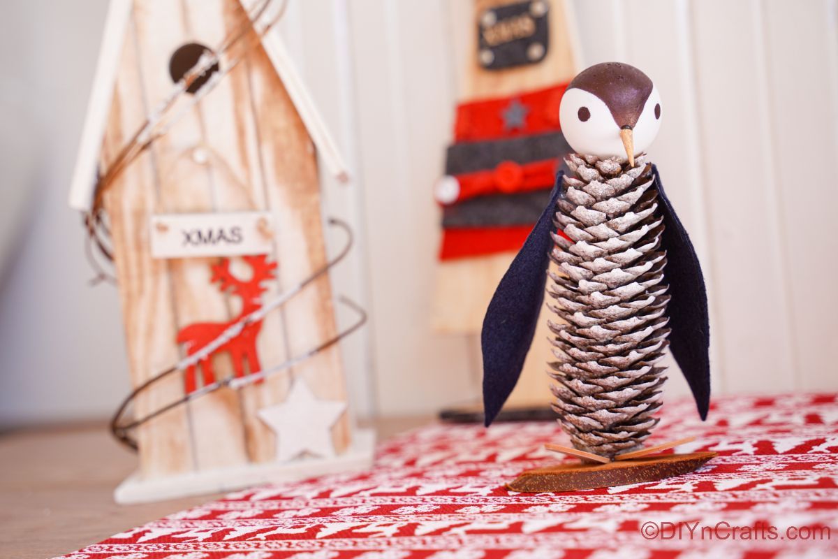 miniaure penguin made of pinecones on red and white paper