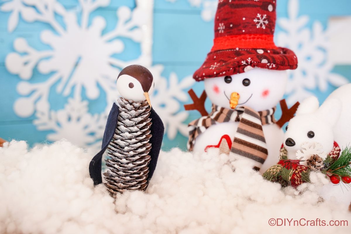 pinecone penguin sitting on fake snow with blue background