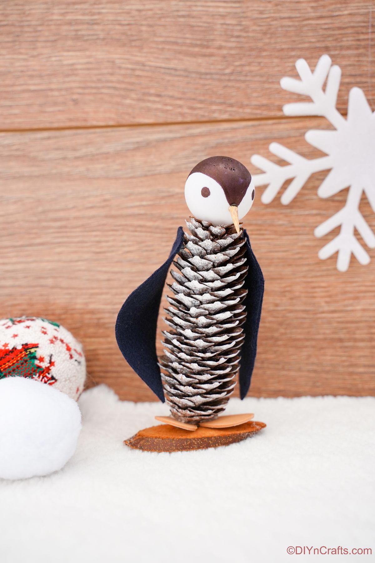 fake penguin made of pinecone in front of wood background