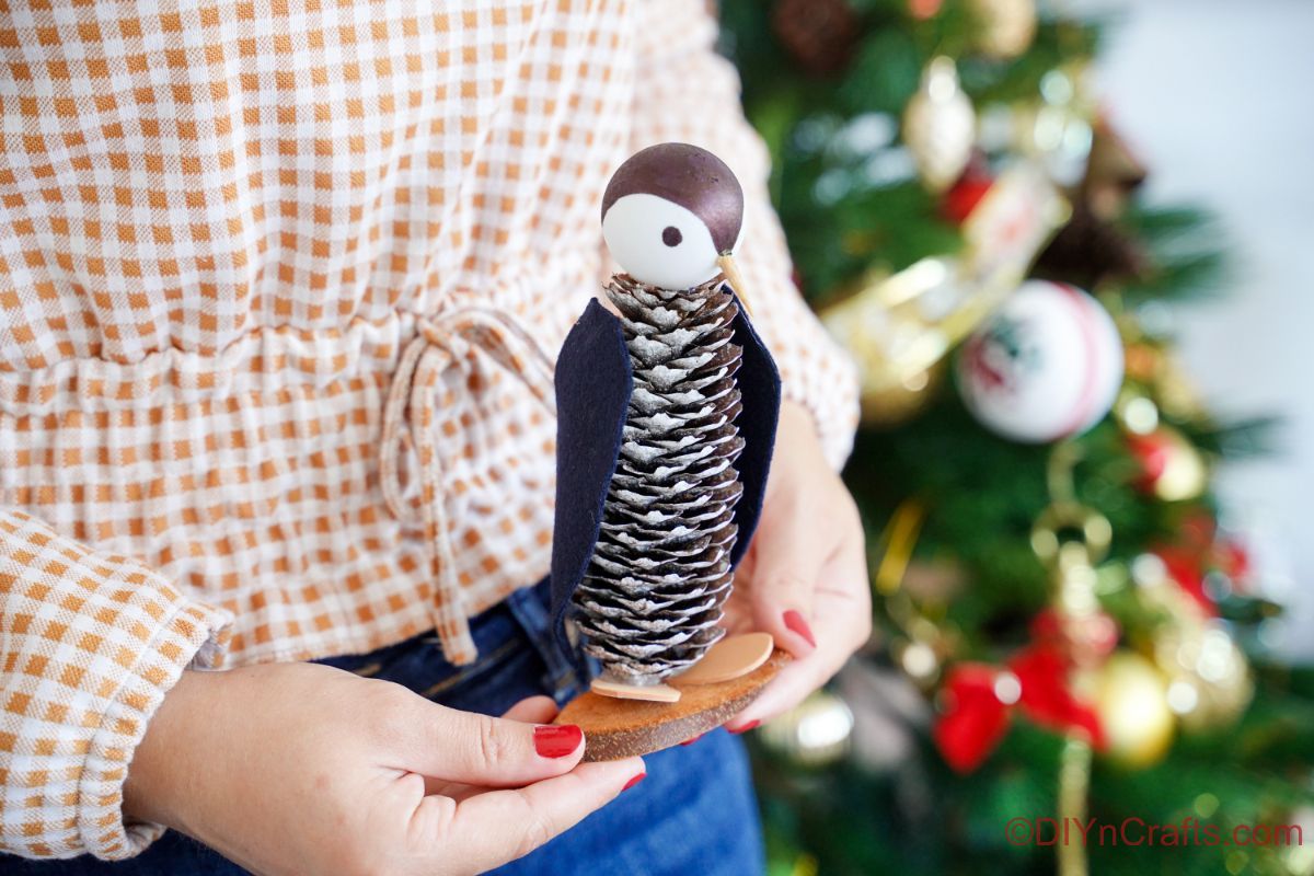Dame tenant un pingouin en face de l'arbre de Noël