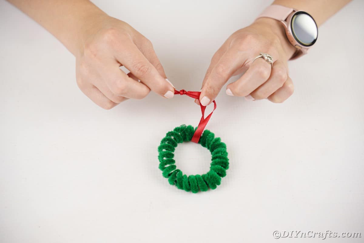 hand adding red ribbon on green wreath ornament